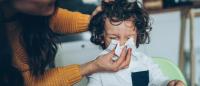 A woman wiping the nose of small child.